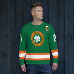 May include: Green and orange hockey jersey with the text "Irish Drinking Team" in a circle with a shamrock and a beer mug. The jersey has white and orange stripes on the sleeves and a white "C" on the right shoulder.