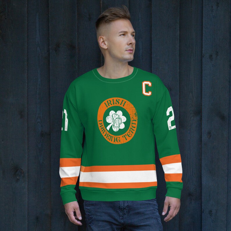 May include: Green and orange hockey jersey with the text "Irish Drinking Team" in a circle with a shamrock and a beer mug. The jersey has white and orange stripes on the sleeves and a white "C" on the right shoulder.
