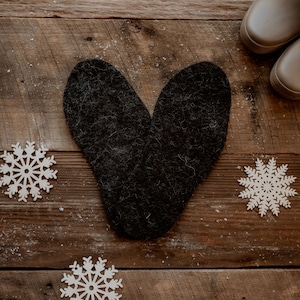 Peut inclure: Une forme de cœur en feutre noir sur un fond en bois avec trois décorations de flocons de neige blancs.