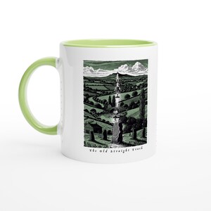 Puede incluir: Taza de cerámica blanca con asa e interior verdes. La taza presenta una ilustración de paisaje en blanco y negro con el texto "the old Straight Track" en la parte inferior. El diseño representa un largo camino a través de un valle.