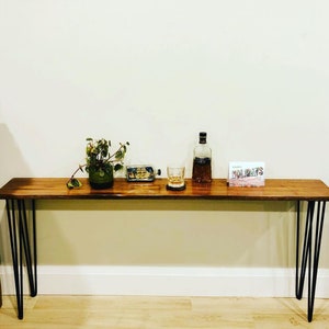 Op de afbeelding: Een houten consoletafel met zwarte haarspeldpoten. De tafel is versierd met een plant in een pot, een glas whisky, een fles sterke drank en een kaart met de tekst "Prettige feestdagen".
