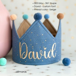 Könnte beinhalten: Eine blaue Stoffkrone mit goldgesticktem Text "David". Die Krone hat eine beige Innenseite und ist mit goldenen Punkten und kleinen Pompons in verschiedenen Farben verziert. Der Text "allmaras" steht unten.