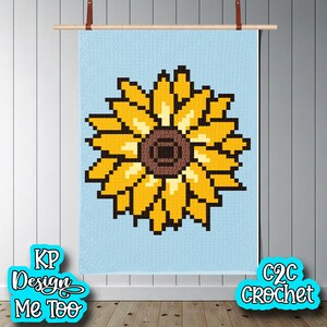 Op de afbeelding: Een pixelig zonnebloemontwerp in geel, bruin en lichtgeel tegen een lichtblauwe achtergrond. Het kunstwerk wordt weergegeven op een houten staaf met leren riemen. De tekst "KP Design Me Too" en "C2C Crochet" zijn zichtbaar.