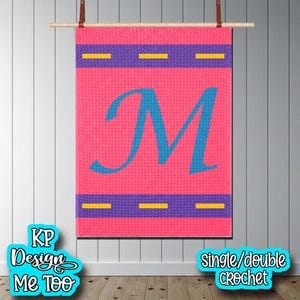 May include: Pink crochet wall hanging with a large blue letter "M". The design includes purple horizontal stripes with yellow dashes. The wall hanging is suspended from a wooden rod with leather straps. The text "KP Design Me Too" is in the lower left.