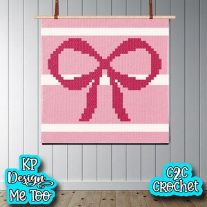 May include: A pink and white crochet wall hanging with a large bow design. The bow is a darker shade of pink than the background, which has horizontal white stripes. The wall hanging is displayed on a wooden rod with leather straps.