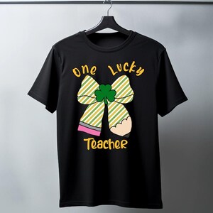 May include: Black t-shirt with a yellow and green striped bow with a shamrock in the center. The text "one lucky teacher" is printed in yellow below the bow.