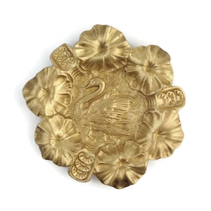 May include: A gold-colored metal trinket dish shaped like a flower with a swan in the center.