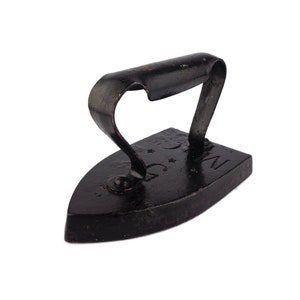 Puede incluir: Una plancha de hierro fundido negra con mango y la palabra "NEW" grabada en la parte inferior.