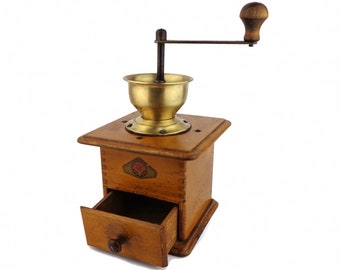 Könnte beinhalten: Eine antike Kaffeemühle aus Holz mit einem Messingbehälter und einer Schublade zum Auffangen des gemahlenen Kaffees. Die Mühle hat einen Holzgriff und eine Metallkurbel.