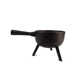 Puede incluir: Caldero de hierro fundido negro con asa y tres patas. El caldero es una pieza decorativa con un acabado rústico.