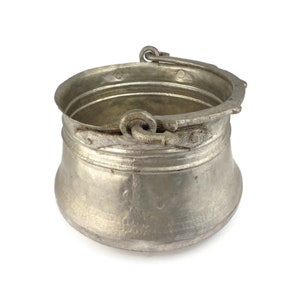 May include: A silver metal cauldron with a hinged handle. The cauldron has a rounded bottom and a wide opening.