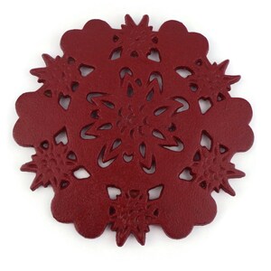 Può includere: Un sottobicchiere rotondo rosso decorativo con un motivo a fiocco di neve. Il sottobicchiere è in pelle e presenta un motivo ritagliato.