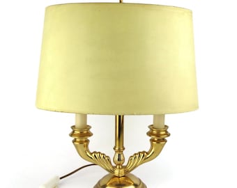 May include: A gold table lamp with a white lampshade. The lamp has a double-arm design with two candle-style bulbs.
