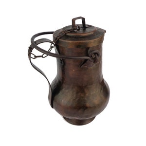 Op de afbeelding: Een vintage koperen kan met een scharnierend deksel en een kettinghendel. De kan heeft een gehamerde afwerking en een donkerbruine patina.