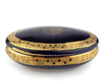 May include: A round, blue and gold trinket box with a floral design. The box is made of porcelain and has a gold rim.