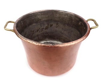 May include: A copper pot with brass handles. The pot is empty and has a worn, aged look.