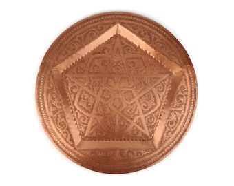 May include: A round copper tray with an intricate star-shaped design. The tray has a raised edge and a smooth, polished surface.