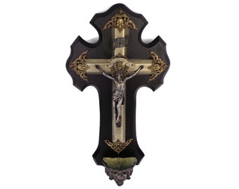 Puede incluir: Un crucifijo de madera negra con detalles dorados y una figura de Jesús plateada. El crucifijo tiene una pequeña copa forrada de verde en la parte inferior.
