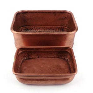 May include: Two copper rectangular containers. The larger container is positioned above the smaller one. Both containers have a rich, reddish-brown colour and a slightly aged appearance. The containers are empty and have rounded corners.