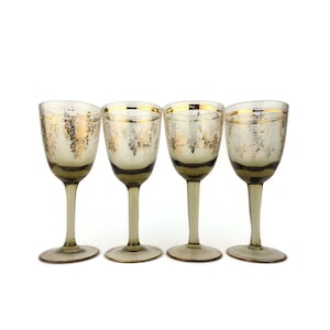 Op de afbeelding: Set van vier heldere glazen shotglazen met bladgoud details en een bruine tint aan de basis.