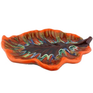 Op de afbeelding: Oranje en bruine keramische serveerschaal in de vorm van een blad met een kleurrijk swirl-ontwerp.