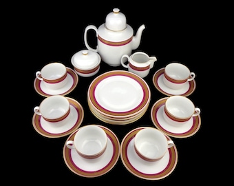 May include: A white porcelain tea set with gold and burgundy trim. The set includes a teapot, creamer, sugar bowl, six cups, and six saucers.