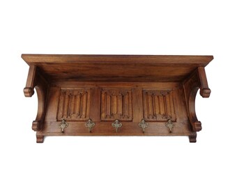 May include: A wooden wall-mounted coat rack with a shelf and decorative carvings. It has six metal hooks and a dark brown finish.
