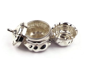 May include: A silver-colored, open container with a lid and a separate, smaller bowl. The container and bowl have a textured, organic design with dark spots. The lid is partially open, revealing the inside of the container. The items are on a white background.