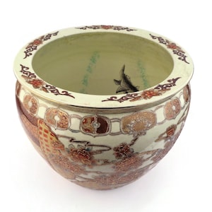 Puede incluir: Una maceta redonda de cerámica color crema con un diseño ornamentado. Presenta una ilustración de pez koi en el interior. El exterior está decorado con patrones florales y geométricos rojos, dorados y marrones.