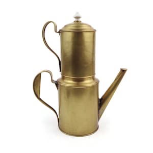 May include: A vintage brass coffee maker with a long spout and two curved handles. The coffee pot has a cylindrical design with a lid and a small white knob on top. The brass has a warm, golden hue.