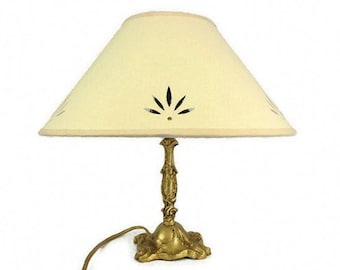 May include: A gold table lamp with a white fabric lampshade featuring a cut-out design. The lampshade is slightly angled.