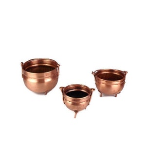 May include: Three copper pots with handles and three legs. The pots are of different sizes and are arranged in a row.