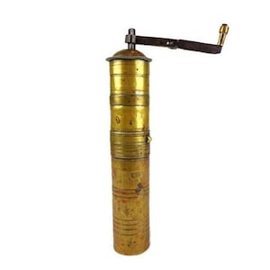 May include: A vintage brass pepper mill with a hand crank. The cylindrical body is made of brass with a tarnished finish, showing signs of age. The crank arm is dark metal, and the handle is brass. The mill is designed for grinding spices.