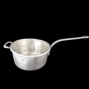 Puede incluir: Un colador de aluminio plateado con un mango largo y pequeños agujeros en toda la parte inferior.