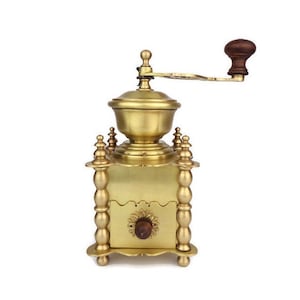 May include: A vintage brass coffee grinder with a wooden handle. The grinder has a decorative design with ornate details and a crank for grinding coffee beans.
