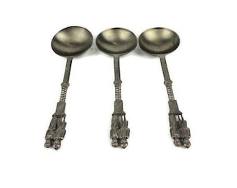 May include: Three silver spoons with ornate handles. The spoons have a rounded bowl and a decorative design on the handle.