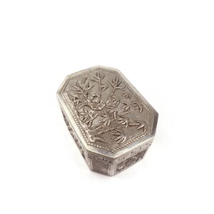 May include: A silver octagonal box with an intricate design of a tree and leaves on the lid.
