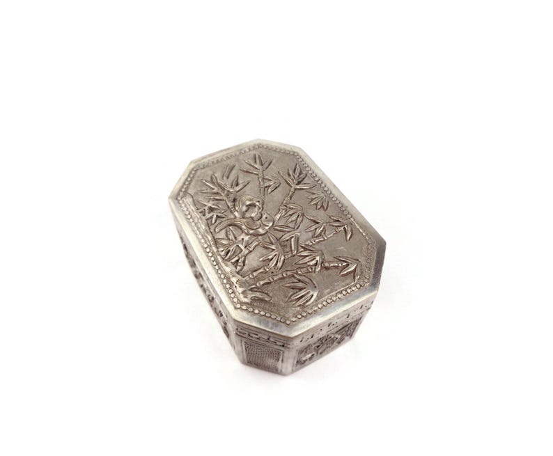 May include: A silver octagonal box with an intricate design of a tree and leaves on the lid.