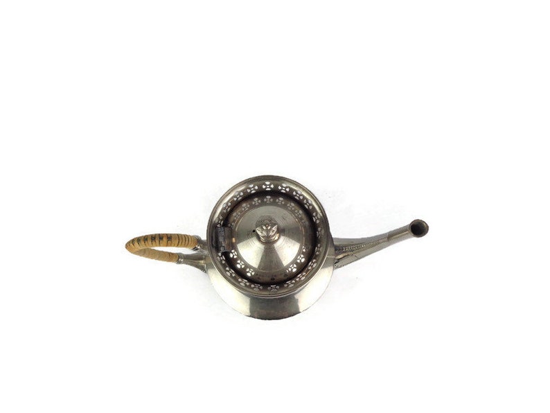 Puede incluir: Una tetera de plata con una tapa decorativa y un asa de madera. La tetera tiene un pico y un cuerpo redondo.