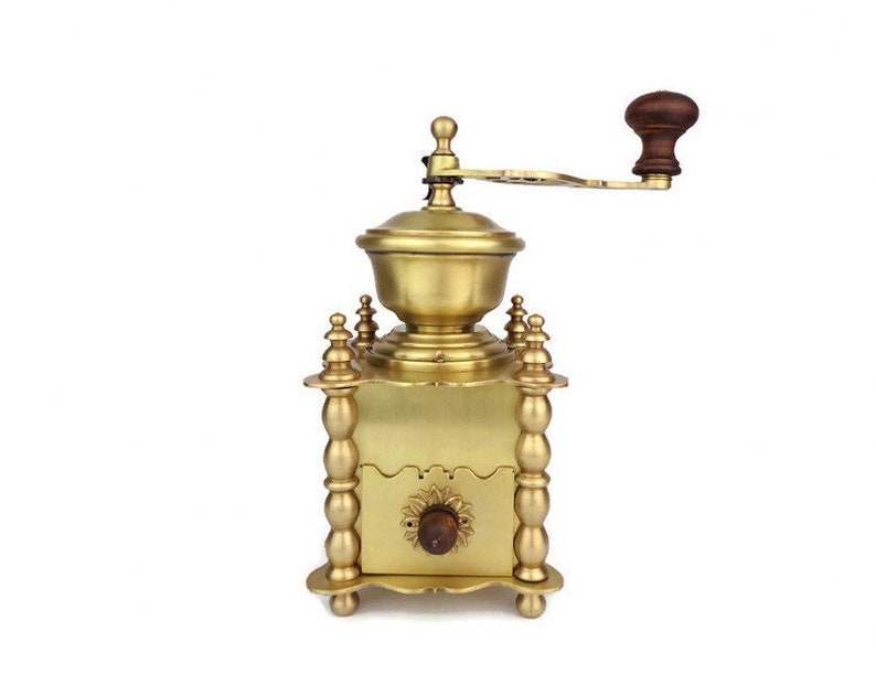 May include: A vintage brass coffee grinder with a wooden handle. The grinder has a decorative design with ornate details and a crank for grinding coffee beans.