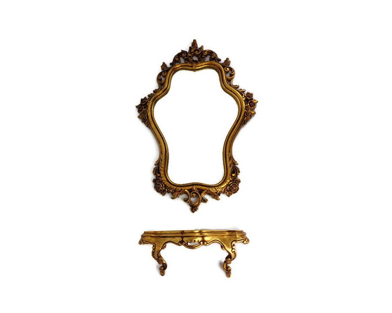 May include: A gold ornate mirror with a decorative frame and a shelf underneath. The mirror is shaped like a teardrop and has a scalloped edge.