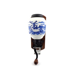 May include: A vintage wall-mounted coffee grinder with a blue and white porcelain jar featuring a windmill scene. The grinder has a wooden base and a metal crank.