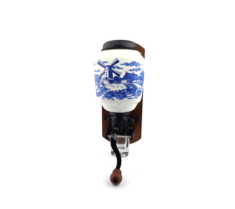 May include: A vintage wall-mounted coffee grinder with a blue and white porcelain jar featuring a windmill scene. The grinder has a wooden base and a metal crank.