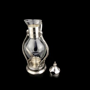 May include: Silver and glass coffee pot with a clear glass carafe and a silver lid. The pot has an ornate design.