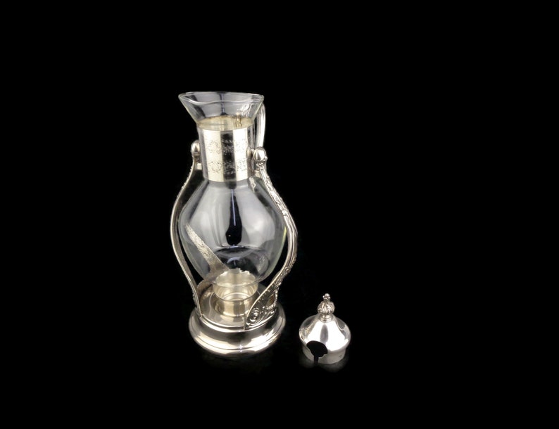May include: Silver and glass coffee pot with a clear glass carafe and a silver lid. The pot has an ornate design.