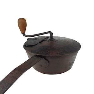 May include: Antique coffee grinder with a wooden handle and a metal body. The grinder has a long handle that extends to the side.