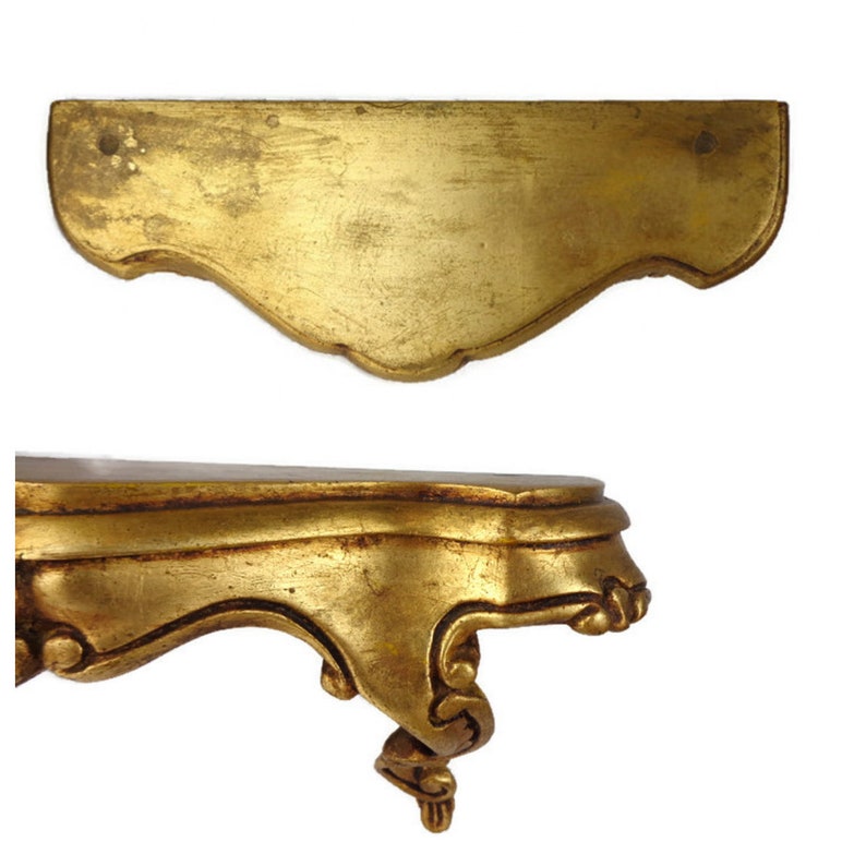 May include: A gold-painted wooden shelf with ornate detailing and a curved front edge. The shelf is supported by a single, intricately carved leg.