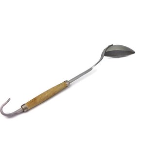 Puede incluir: Un cucharón de plata con mango de madera y un gancho en el extremo. El cucharón está diseñado para sacar líquidos.