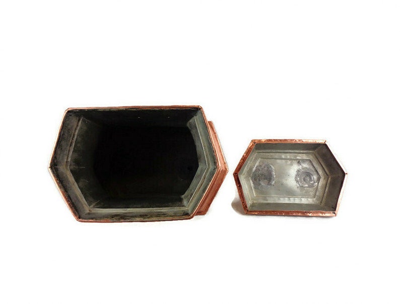 May include: A copper-colored hexagonal box with a lid. The box is open and the inside is lined with a silver-colored material.