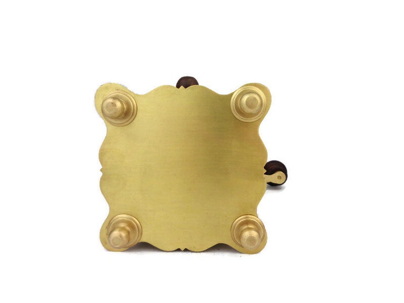 May include: A gold metal stand with four feet and a decorative design. The stand has a round top and a small wooden handle.